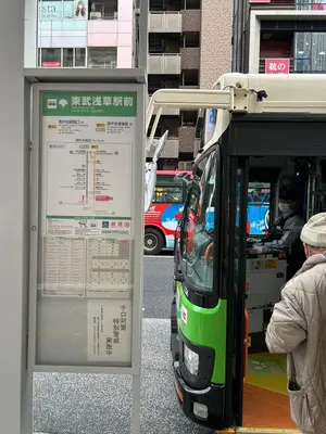a bus stop with a sign next to a bus at \u6d45\u8349\u30b9\u30ab\u30a4\u30ac\u30fc\u30c7\u30f3\u30db\u30c6\u30eb in Tokyo