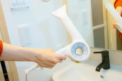 a person is holding a hair dryer over a sink at Fox & Fortune 4A -Nomad Stay- 3-min Walk, PS5, Apple Studio in Tokyo