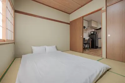 a bedroom with a large white bed and a kitchen at self-check in-shinjuku-windhouse in Tokyo