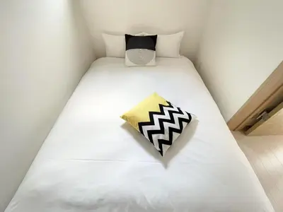 a white bed with a black and white pillow on it at COMMA HOUSE Kitaikebukuro 101 in Tokyo