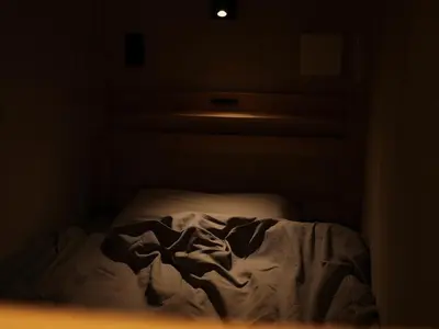 an unmade bed in a dark room at Dogen sauna&stay in Tokyo