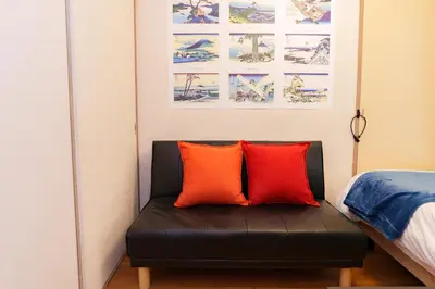 a black couch with two orange pillows in a bedroom at \u30aa\u30fc\u30d7\u30f3\u7279\u4fa1 \u5317\u658e \u5bcc\u58eb\u306e\u9593 \u6c60\u888b4\u5206 \u65b0\u5bbf16\u5206 \u6e0b\u8c3721\u5206 in Tokyo