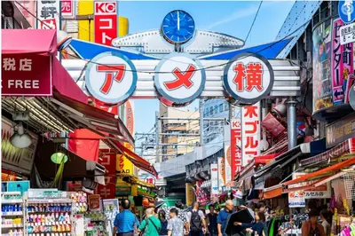 a street with people walking through a market with signs at \u65b0\u4e0a\u91ce202 \u7ad9\u6b65\u884c7\u5206\u949f\u7a3b\u6210\u753a\u7ad92\u5206\u949f in Tokyo