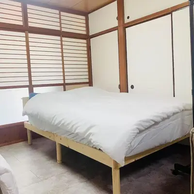 a bedroom with a bed with white sheets and windows at Japan House \u6e6f\u5cf6 in Tokyo