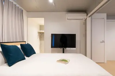 a bedroom with a white bed with blue pillows and a tv at Bel Avenir in Tokyo