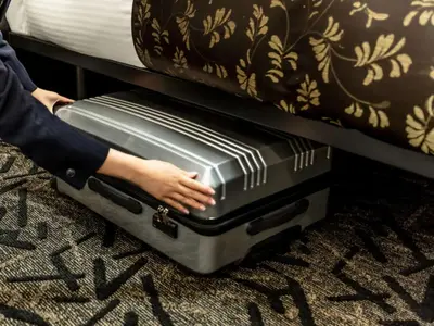 a person is holding a suitcase under a bed at APA Hotel Suidobashi Ekimae in Tokyo