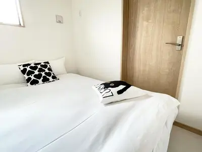 a white bed with a black and white shirt on it at Comma House Kitaikebukuro 301 in Tokyo