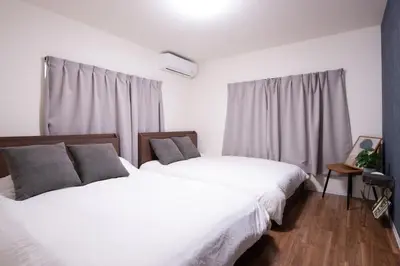two beds in a bedroom with white sheets and gray pillows at Fullhouse 102 in Tokyo
