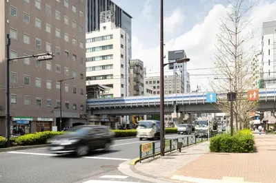 a car driving down a city street with a train on a bridge at Maison Miyashita in Tokyo