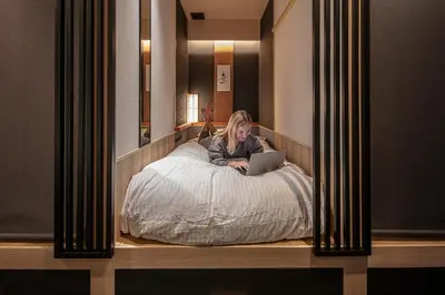 a woman sitting on a bed with a laptop at ENSO TOKYO Akasaka in Tokyo