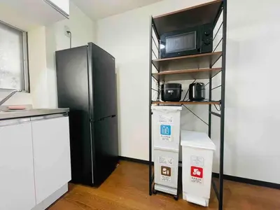 a kitchen with a black refrigerator and a shelf with a microwave at \u7573\u306e\u9593\u6c60\u888b in Tokyo