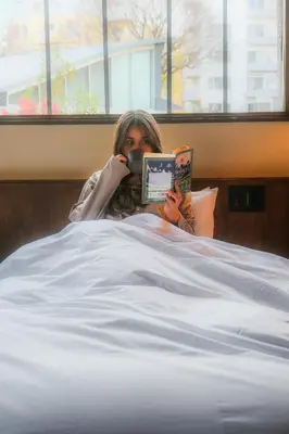 a woman laying in bed reading a book and talking on a cell phone at HOTEL RIN TOKYO - Private Townhouse - in Tokyo