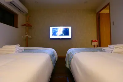 two beds in a room with a tv on the wall at 101 Convenient Ueno Lucky Yado in Tokyo