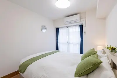 a bedroom with a bed with white sheets and green pillows at 3 bedrooms, 5-minute walk to Shinjuku City Center, Isetan department store , max 7 people in Tokyo
