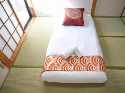 a small bed in a room with a red pillow at Two bathrooms, two toilets 6 mins walking distance from Keisei Takasago Station in Tokyo