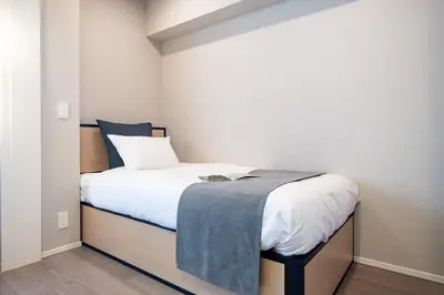 a small bedroom with a bed with a blue blanket on it at \u30a2\u30fc\u30d0\u30cd\u30c3\u30af\u30b9\u99d2\u8fbc in Tokyo