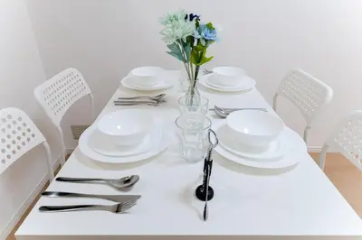 a white table with white plates and a vase of flowers at A quiet residential street with a 5-minute walk from Shirokane Takanawa Station! in Tokyo