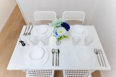 a white table with plates and glasses and a vase with flowers at A quiet residential street with a 5-minute walk from Shirokane Takanawa Station! in Tokyo