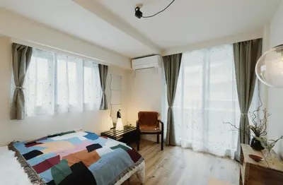 a bedroom with a bed and a chair and windows at The Apartment Hotel Shibuya 2 in Tokyo