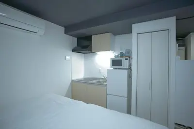 a small white kitchen with a bed and a microwave at Yoyogi Park Retreat in Tokyo