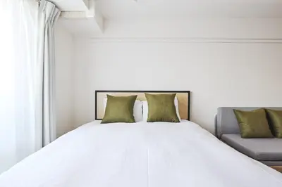 a white bed with two green pillows and a couch at \u30b3\u30b9\u30e2\u30ea\u30fc\u30c9\u5e61\u30f6\u8c37 in Tokyo