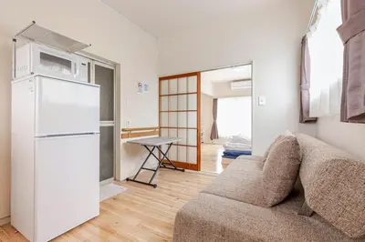 a living room with a couch and a white refrigerator at tkm\u5317\u5c0f\u5ca91\u4e01\u76ee201 in Tokyo