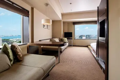 a hotel room with a couch and a desk and a large window at Urayasu Brighton Hotel Tokyo Bay in Urayasu