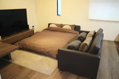 a bedroom with a bed and a couch and a flat screen tv at IKEPOND HOUSE Tokyo in Tokyo