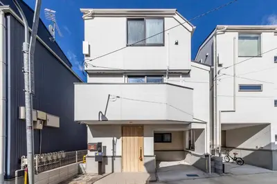 a white house with a wooden door on a street at Akabanenishi 3chome House in Tokyo