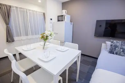 a white dining room table with white chairs and a white refrigerator at \u5927\u4e45\u4fdd\u30b3\u30ea\u30a2\u30f3\u30bf\u30a6\u30f3\u76f4\u901a \u5317\u65b0\u5bbf\u306e\u30e2\u30c0\u30f3\u30b2\u30b9\u30c8\u30cf\u30a6\u30b9 YoYi in Tokyo