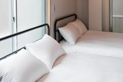 two beds with white pillows sitting next to a window at Sunshine Inn 456 - Economic APT in Tokyo Tranquil Block, with Direct Access to Ginza & Akihabara in Tokyo