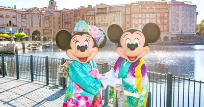 two mickeys dressed in costumes standing next to a fence at Coco Aoto in Tokyo