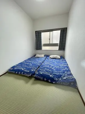 a bedroom with a bed with a blue comforter and a window at \u8c4a\u5cf6\u5927\u585a\u3055\u304f\u3089\u6c11\u6cca in Tokyo