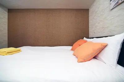 a white bed with two orange pillows on it at Best Value 2BR that Sleep 6, Quiet neighborhood, Close to Metro in Tokyo