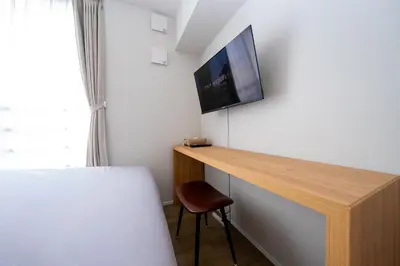 a bedroom with a desk with a tv on a wall at ZAITO Waseda Terra Hotel in Tokyo