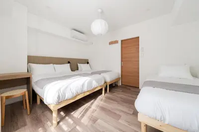 two beds in a room with white walls and wooden floors at Second Home SHINJUKU in Tokyo
