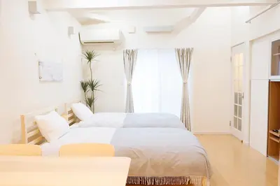 a white bedroom with two beds and a window at Dori Dori House Ebisu in Tokyo