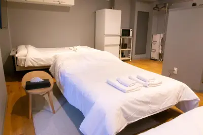 a room with two beds with white sheets and a chair at \u30a8\u30b3\u30ed\u65b0\u5bbf\u7b2c\u4e8c\u30d3\u30eb in Tokyo
