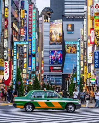 a green car driving down a busy city street at Shinjuku city\u897f\u65b0\u5bbf in Tokyo