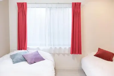 a bedroom with two beds and a window with red curtains at The underz suite residence Ikebukuro by Tranova in Tokyo