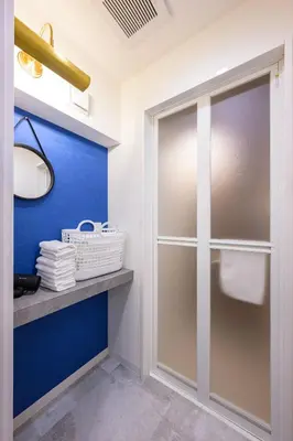 a bathroom with a glass shower door and a blue wall at TOMARU Meguro in Tokyo