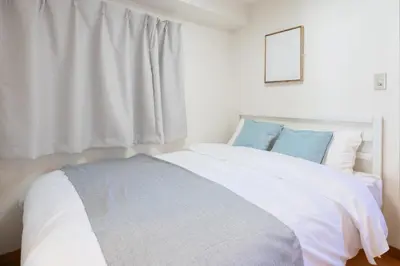 a bedroom with a white bed with blue pillows at \u6771\u771f\u30d3\u30eb2\u968e \u7b39\u585a\u99c5\u304b\u3089\u5f92\u6b694\u5206 in Tokyo