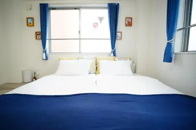 two beds in a bedroom with blue curtains and a window at Tomo House Oshiage - from 2 minutes station \u62bc\u4e0a \u99c5\u304b\u3089\u5f92\u6b692\u5206 in Tokyo