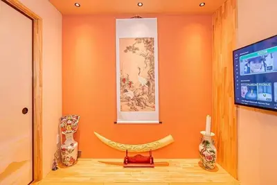a room with an orange wall with a tv and vases at My Sumida Home A in Tokyo