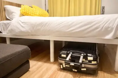 a suitcase under a bed with a white sheet at UPHouse 2C Gotokuji in Tokyo