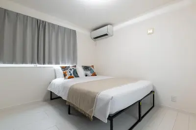 a bed in a white room with a window at Conveniently located 10 min walk from Shin-Okubo Station and 7 min walk from Higashi-Shinjuku Station -Okubo hosuse- in Tokyo