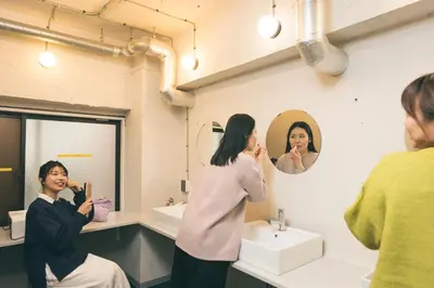 a woman brushing her teeth in front of a bathroom mirror at Imano Tokyo Hostel in Tokyo