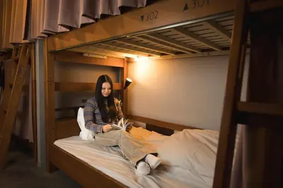 a woman sitting on a bunk bed reading a book at Imano Tokyo Hostel in Tokyo
