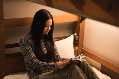 a woman sitting on a bed reading a book at Imano Tokyo Hostel in Tokyo