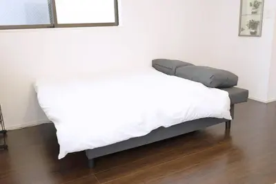 a bed in a room with a white blanket on it at Happy Home \u6771\u5341\u6761\u99c5\u5f92\u6b697\u5206 \u5341\u6761\u99c5\u3088\u308a\u6c60\u888b\u99c5\u76f4\u901a5\u5206 \u5b50\u3069\u3082\u5927\u559c\u3073\u306e\u6ed1\u308a\u53f0\u3068\u7121\u6599\u99d0\u8eca\u5834\u4ed8\u304d\u4e00\u8ed2\u5bb6 in Tokyo